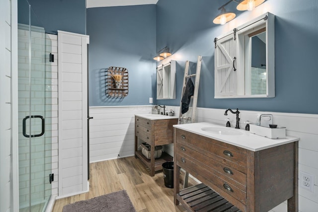 full bath with a wainscoted wall, wood finished floors, a sink, and a stall shower