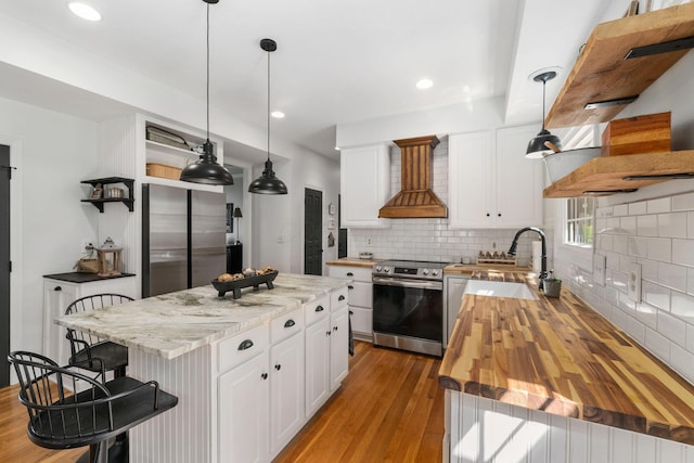 kitchen featuring open shelves, a breakfast bar, wood counters, appliances with stainless steel finishes, and custom range hood