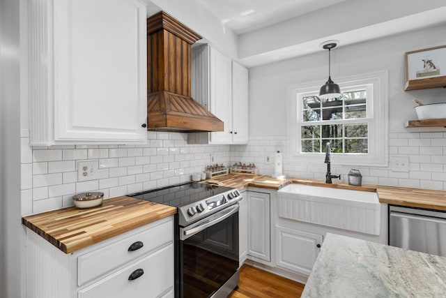 kitchen featuring butcher block counters, decorative backsplash, appliances with stainless steel finishes, custom exhaust hood, and white cabinetry