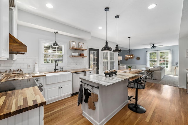 kitchen featuring open shelves, butcher block counters, stainless steel dishwasher, and a sink