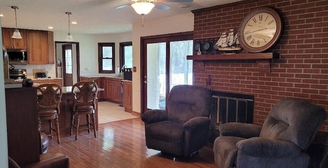 living room featuring a brick fireplace, light hardwood / wood-style flooring, and ceiling fan