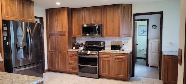 kitchen featuring light stone countertops, light wood-type flooring, backsplash, and stainless steel appliances