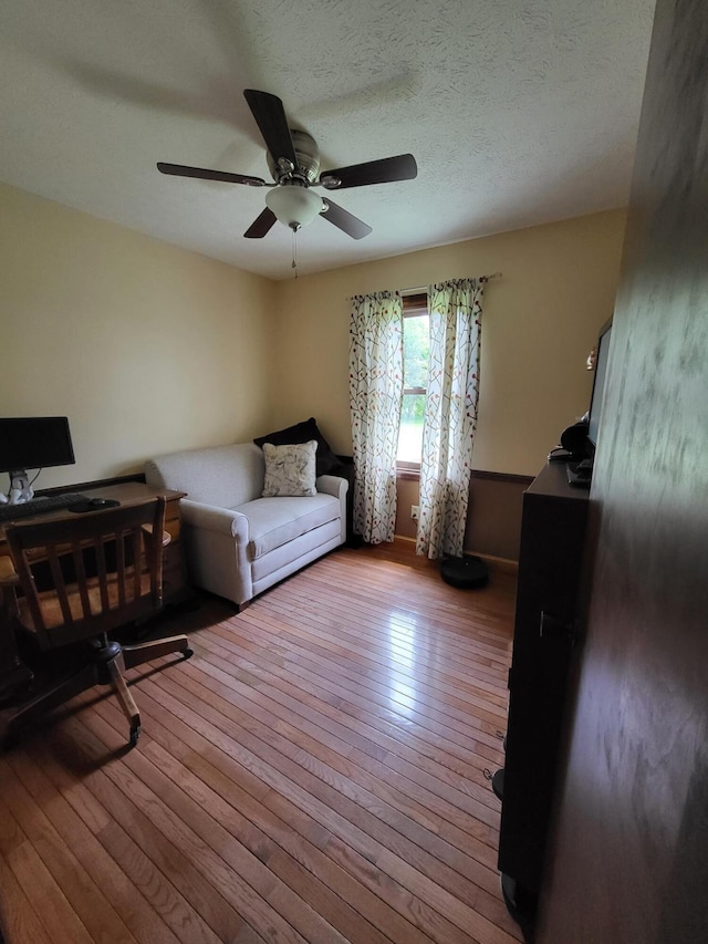 living room with ceiling fan, light hardwood / wood-style flooring, and a textured ceiling