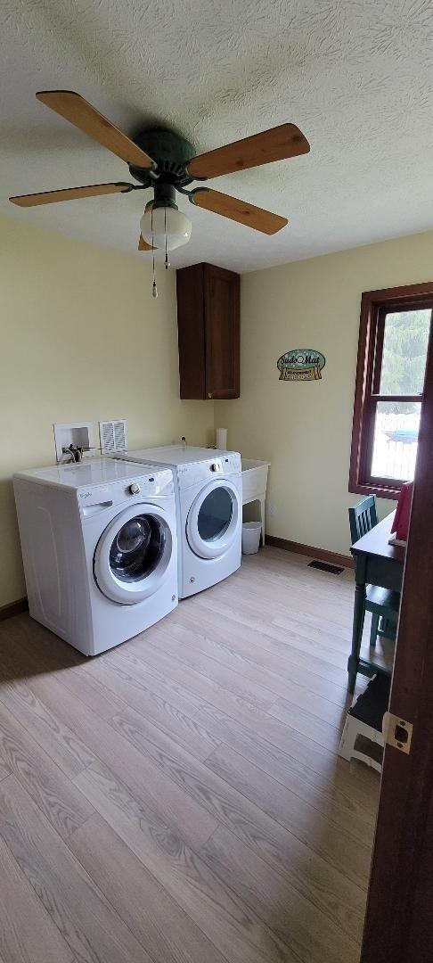 laundry room with washer and clothes dryer, cabinets, light wood-type flooring, and a textured ceiling