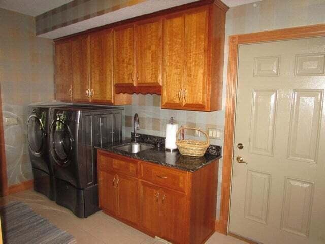 clothes washing area featuring light tile patterned floors, washing machine and dryer, sink, and cabinets