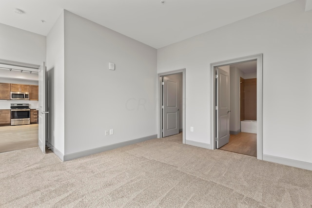 unfurnished bedroom with light colored carpet, a spacious closet, and ensuite bathroom