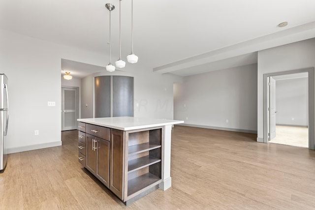 kitchen featuring hanging light fixtures, stainless steel fridge, light wood-type flooring, a kitchen island, and dark brown cabinetry