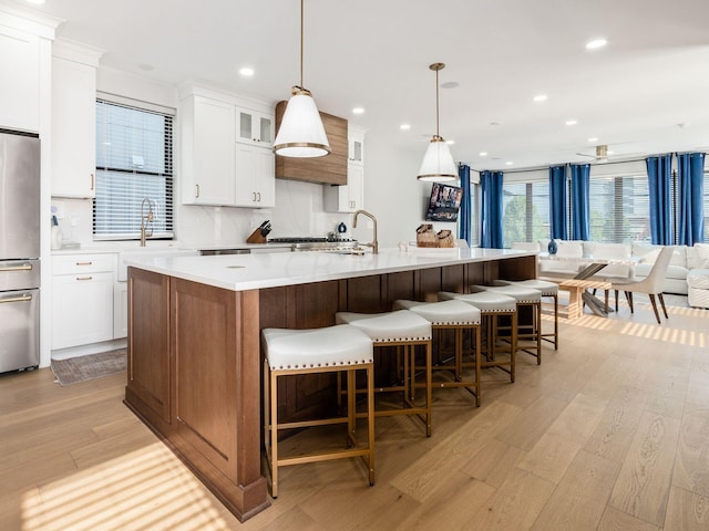 kitchen featuring a large island with sink, light wood-type flooring, decorative light fixtures, and stainless steel refrigerator