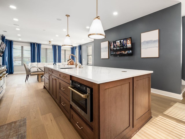 kitchen featuring sink, a center island with sink, light hardwood / wood-style flooring, oven, and hanging light fixtures