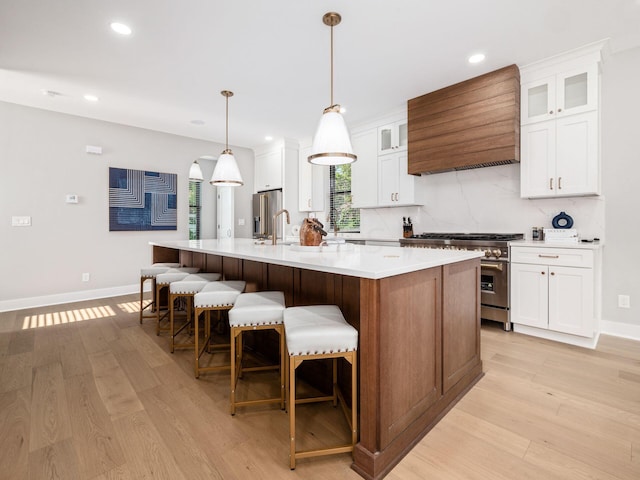 kitchen featuring appliances with stainless steel finishes, premium range hood, light hardwood / wood-style flooring, white cabinets, and a large island