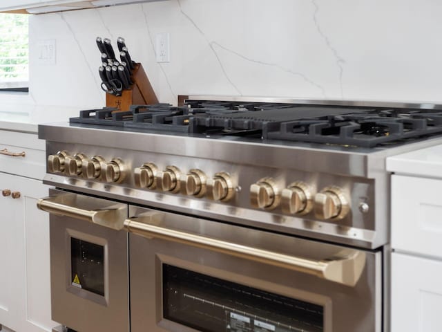 interior details with range with two ovens, light stone counters, and white cabinetry