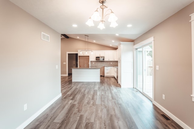 kitchen featuring pendant lighting, lofted ceiling, a kitchen island, white cabinetry, and a chandelier