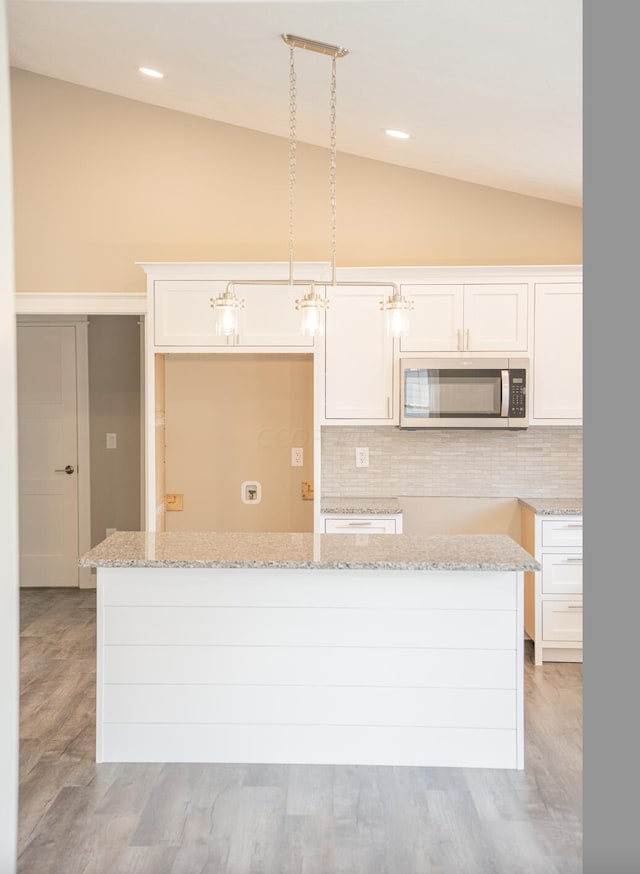 kitchen featuring white cabinets, decorative light fixtures, light wood-type flooring, and vaulted ceiling