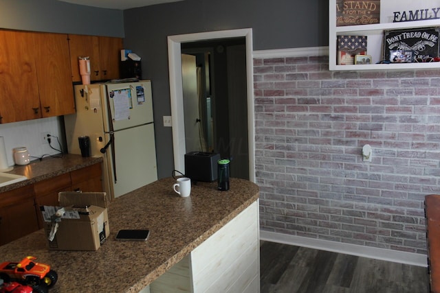 kitchen with white fridge, dark wood-type flooring, and brick wall