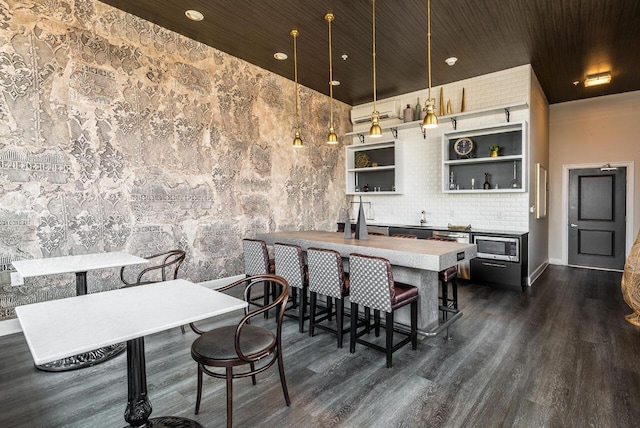 kitchen featuring a breakfast bar, stainless steel microwave, an AC wall unit, hanging light fixtures, and dark hardwood / wood-style floors