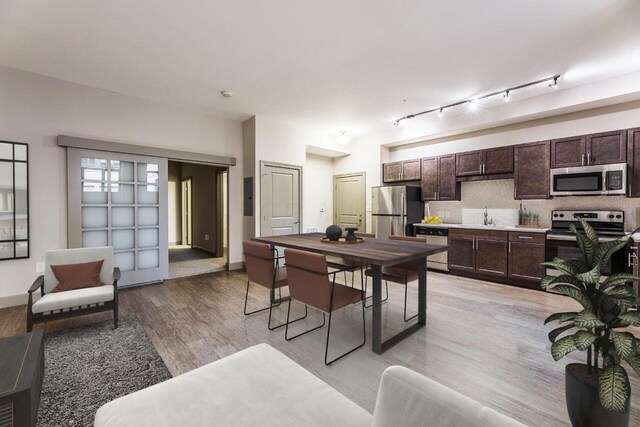 kitchen with appliances with stainless steel finishes, light wood-type flooring, track lighting, dark brown cabinetry, and sink