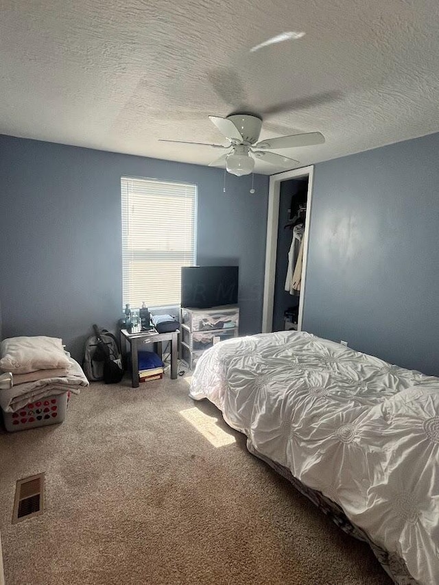 bedroom featuring carpet flooring, ceiling fan, a textured ceiling, a walk in closet, and a closet