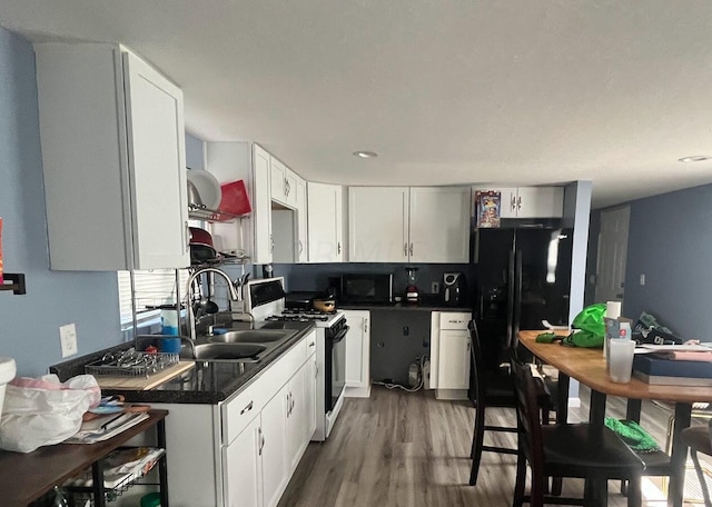 kitchen with white cabinets, black fridge, sink, white gas stove, and wood-type flooring