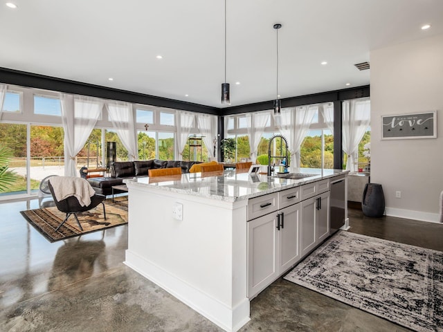 kitchen featuring sink, light stone counters, an island with sink, decorative light fixtures, and white cabinets