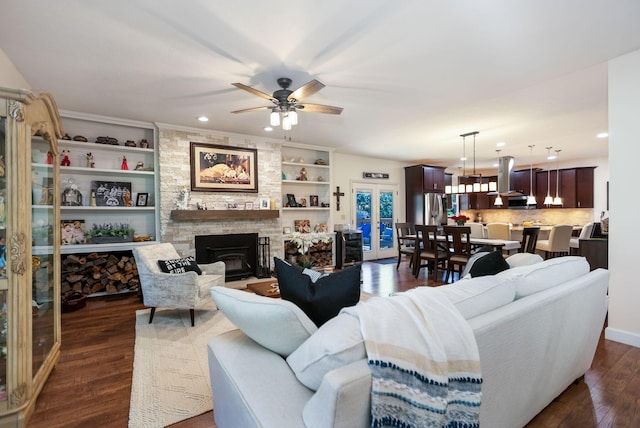 living room with a fireplace, built in shelves, dark hardwood / wood-style flooring, and ceiling fan