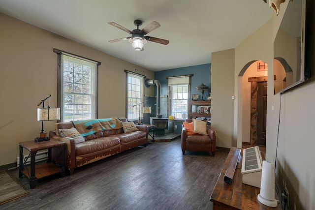 living room featuring a wood stove, ceiling fan, and dark wood-type flooring