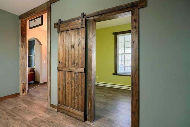 hall with a barn door, wood-type flooring, and baseboard heating