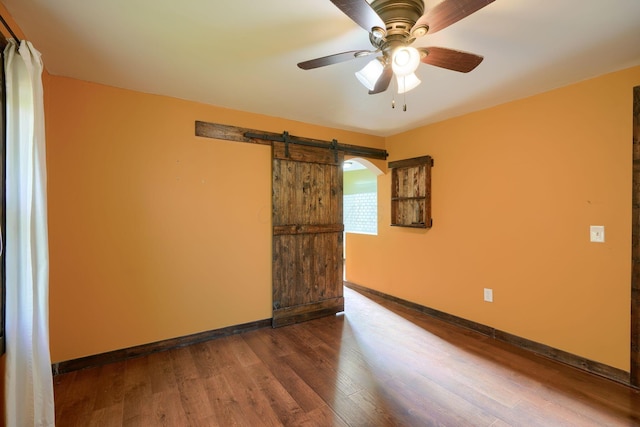 empty room featuring ceiling fan, a barn door, and dark wood-type flooring