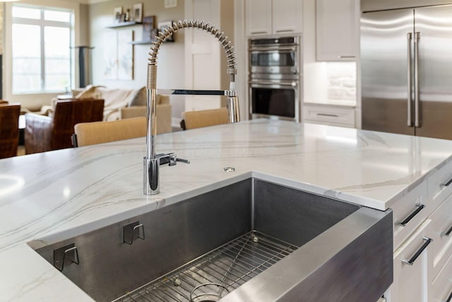 kitchen with white cabinets, a sink, open floor plan, light stone countertops, and stainless steel appliances