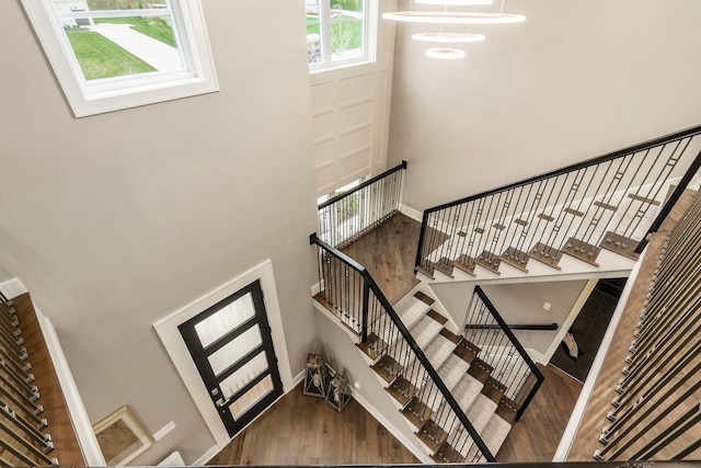 stairway featuring baseboards, a towering ceiling, and wood finished floors
