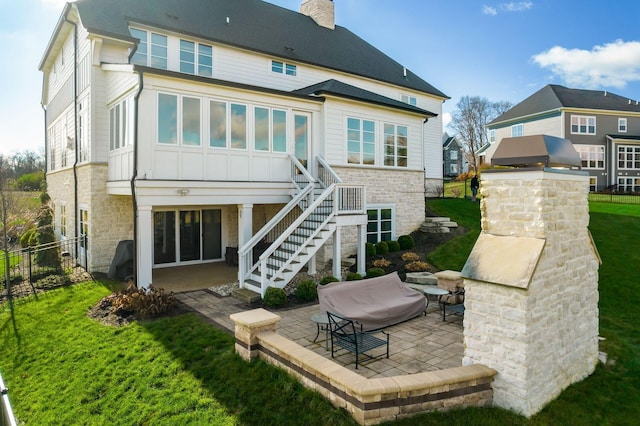 rear view of property featuring a patio area, a yard, stone siding, a chimney, and fence