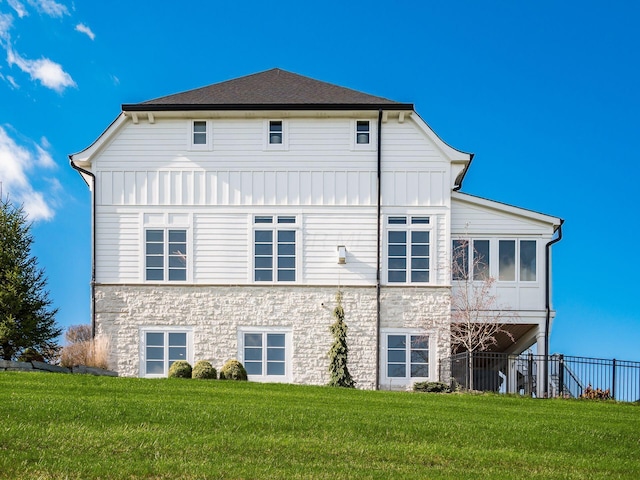 back of property featuring board and batten siding, stone siding, and a lawn