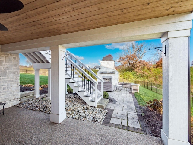 view of patio featuring exterior fireplace, fence, and stairs