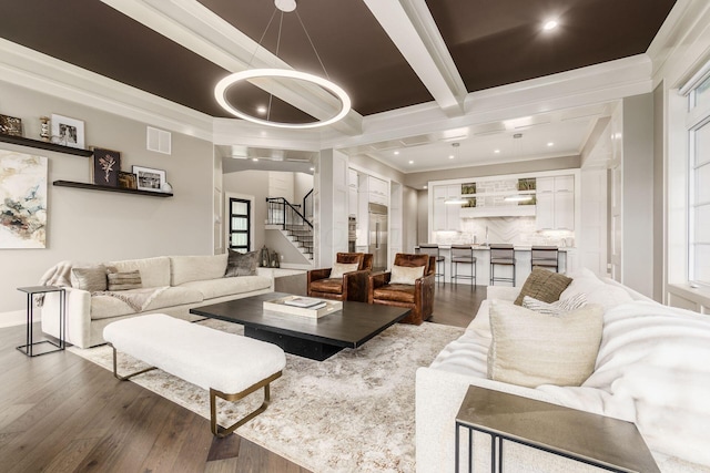 living area with visible vents, ornamental molding, beamed ceiling, wood finished floors, and stairs