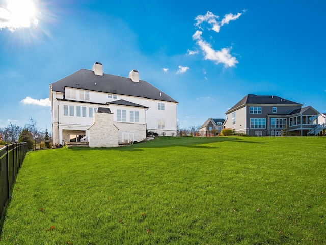 rear view of property with a chimney, fence, and a lawn