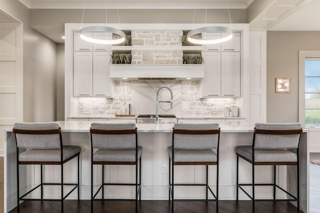 kitchen with dark wood finished floors, a kitchen island with sink, white cabinetry, and decorative backsplash