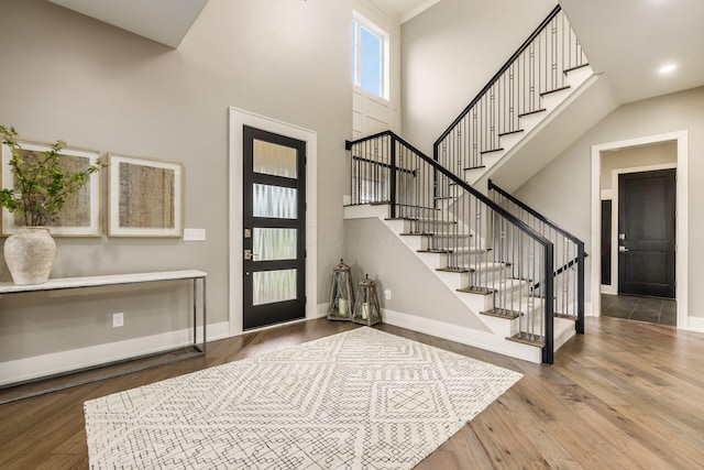 entrance foyer featuring baseboards, wood finished floors, a towering ceiling, and stairs