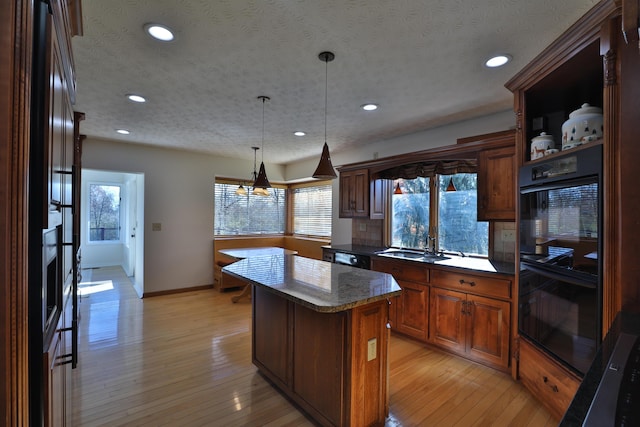 kitchen with decorative light fixtures, light hardwood / wood-style flooring, a kitchen island, and black double oven