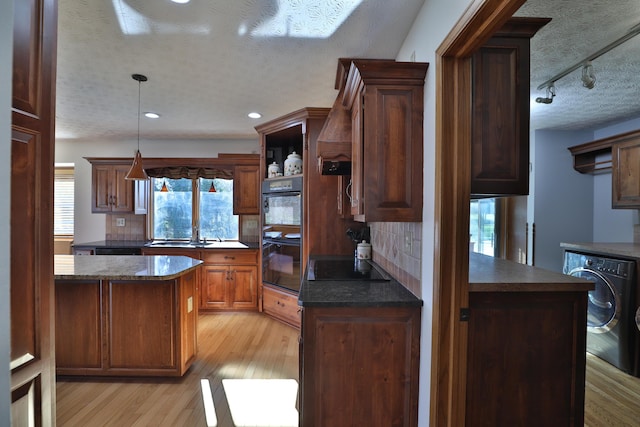 kitchen with light wood-type flooring, tasteful backsplash, a textured ceiling, black appliances, and washer / dryer