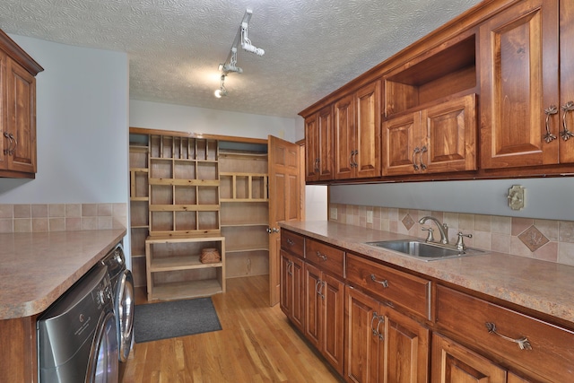 kitchen featuring backsplash, sink, light hardwood / wood-style flooring, washing machine and dryer, and a textured ceiling