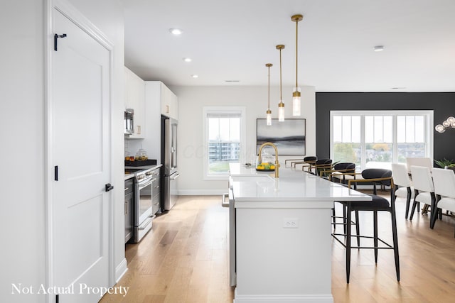 kitchen with a breakfast bar area, an island with sink, light hardwood / wood-style floors, white cabinetry, and stainless steel appliances