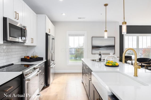 kitchen featuring appliances with stainless steel finishes, sink, decorative light fixtures, white cabinets, and light hardwood / wood-style floors