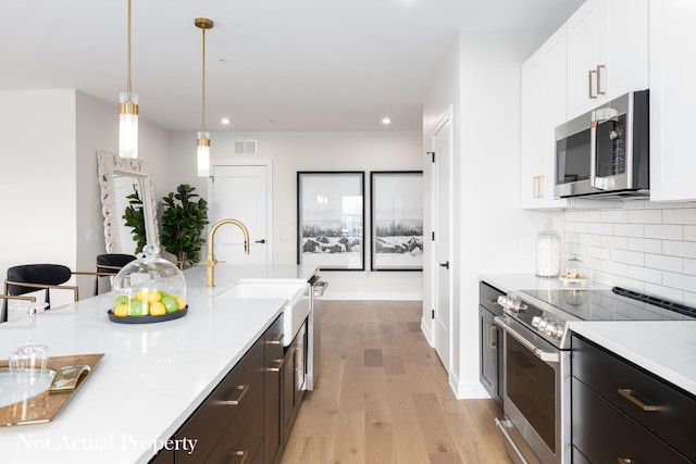 kitchen with decorative backsplash, decorative light fixtures, light hardwood / wood-style floors, white cabinetry, and stainless steel appliances