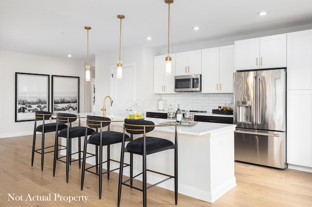 kitchen featuring a kitchen island with sink, pendant lighting, light wood-type flooring, and appliances with stainless steel finishes