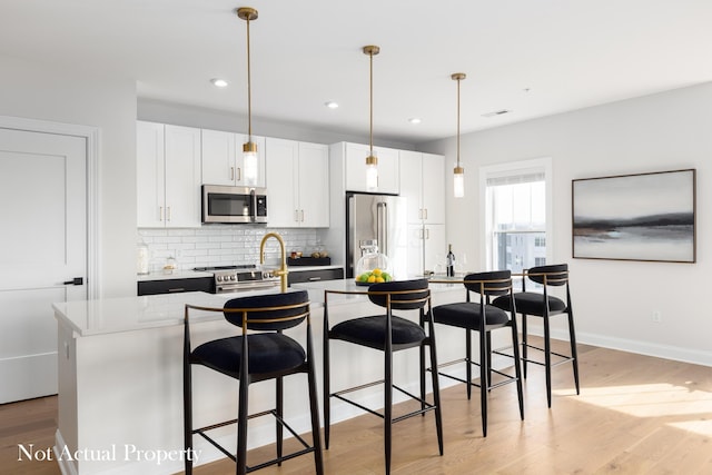 kitchen featuring hanging light fixtures, stainless steel appliances, white cabinetry, and a kitchen island with sink