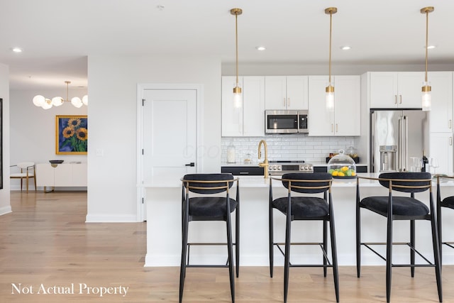 kitchen with stainless steel appliances, a kitchen island with sink, decorative light fixtures, light hardwood / wood-style flooring, and white cabinetry