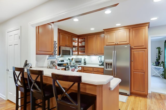 kitchen featuring a breakfast bar, appliances with stainless steel finishes, kitchen peninsula, and light wood-type flooring