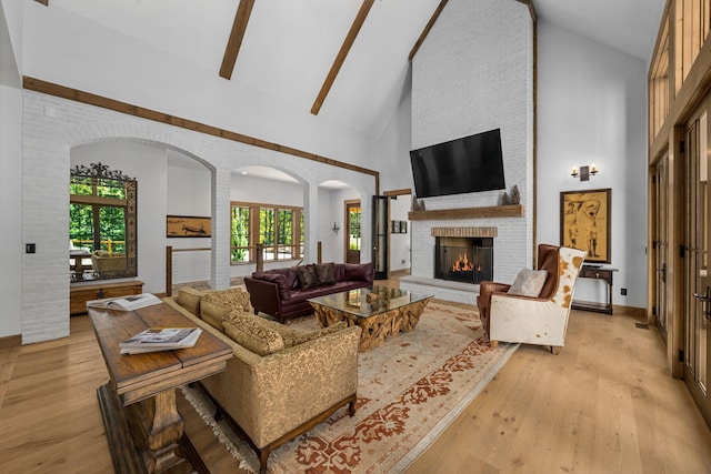 living room featuring a brick fireplace, high vaulted ceiling, and light hardwood / wood-style flooring