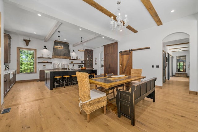 dining space featuring sink, a barn door, light hardwood / wood-style flooring, a notable chandelier, and beamed ceiling