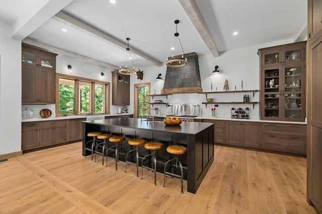 kitchen featuring beam ceiling, light hardwood / wood-style flooring, an island with sink, a breakfast bar, and custom exhaust hood