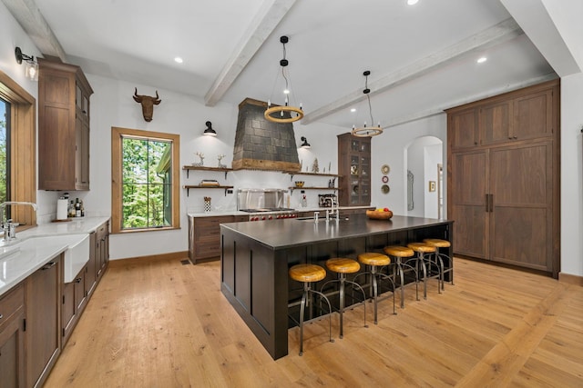 kitchen featuring a large island, sink, light hardwood / wood-style flooring, beamed ceiling, and a breakfast bar